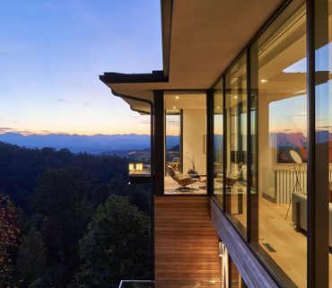 Modern villa with lots of glass, looking out over Californian mountains at nightfall.