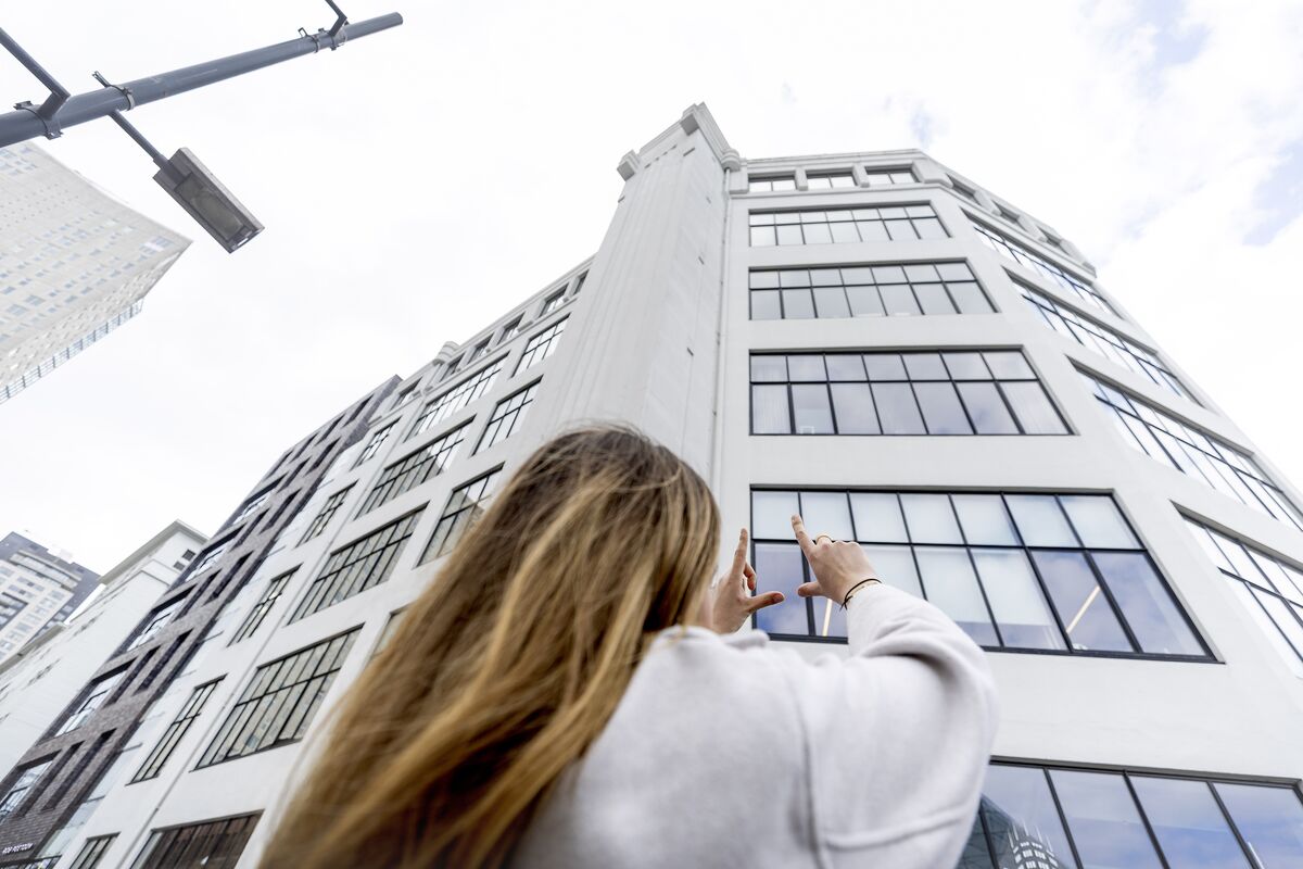 Donna che alza le mani verso un edificio bianco di media altezza con molte finestre.