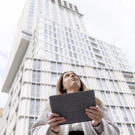 Donna bionda con iPad in mano che guarda verso un edificio residenziale bianco.