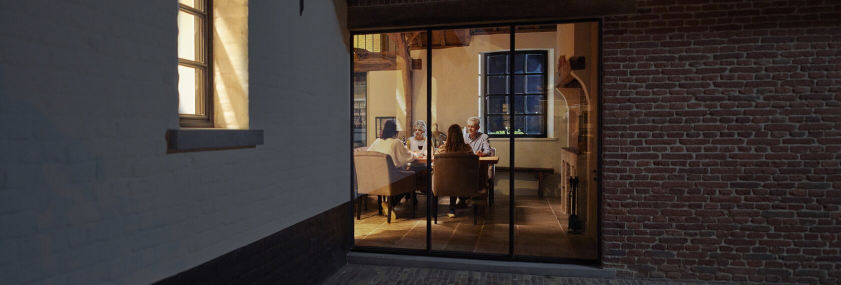 Family sitting at table behind large window at night.