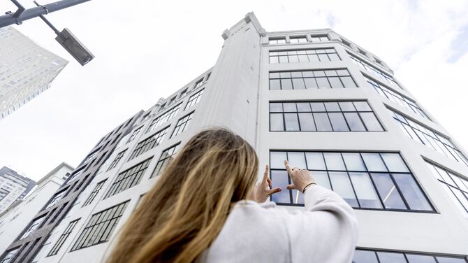 Donna con le mani alzate verso un edificio bianco di media altezza con molte finestre.