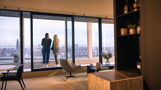 Vista interna di un appartamento moderno con ampie porte scorrevoli e due persone sul balcone.