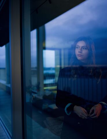 Donna che guarda fuori dalla finestra al calar della notte.